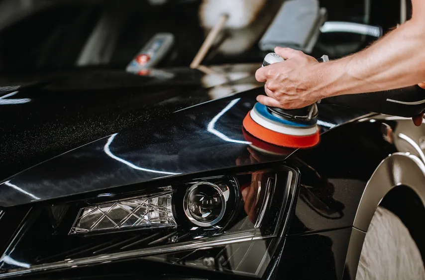A detailer using an orbital polisher on dark vehicle paint