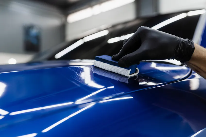 A gloved hand applying ceramic coating to blue vehicle paint with an applicator