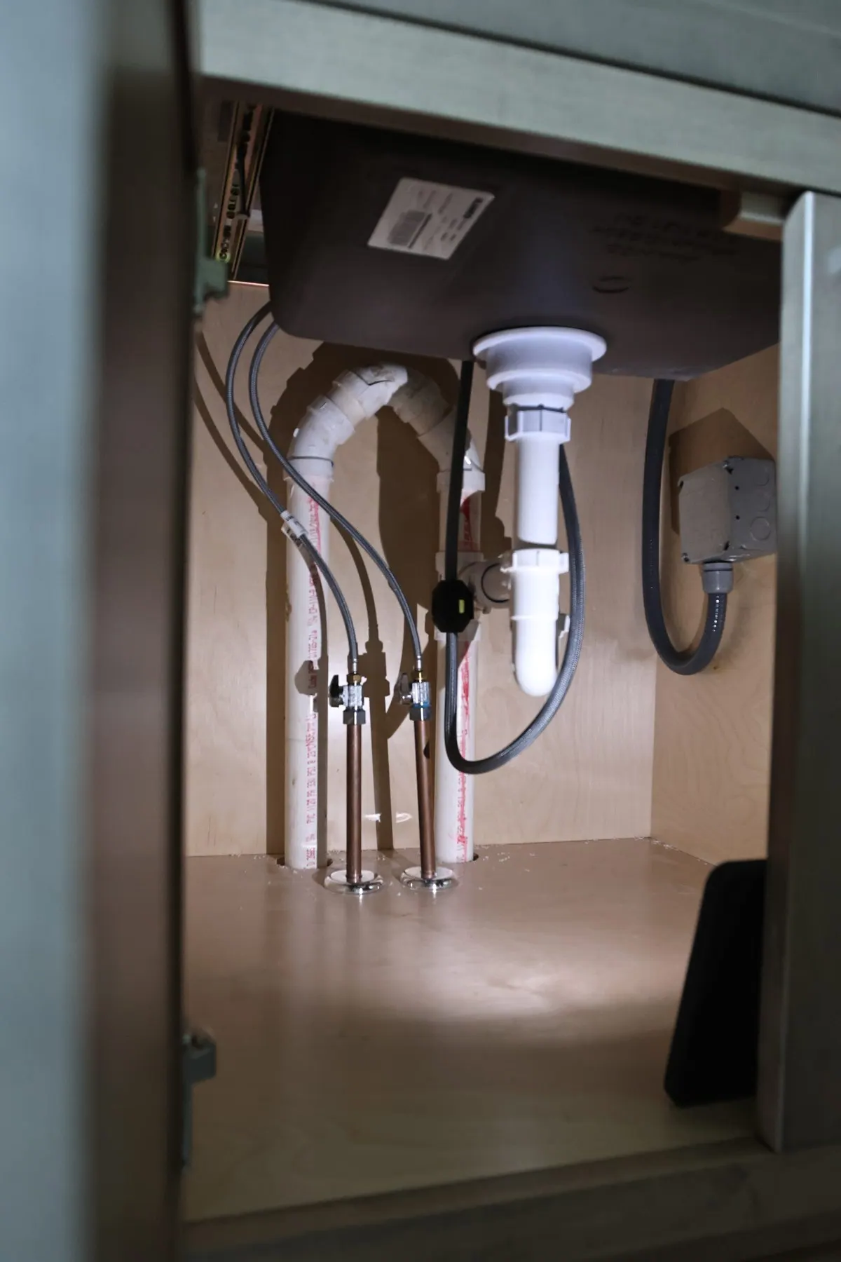 Drain piping, supply connections and a disposal beneath a kitchen sink.