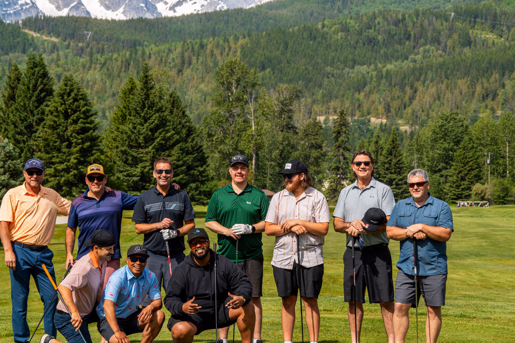 A group of golfers posing on the fairway with forested mountains behind