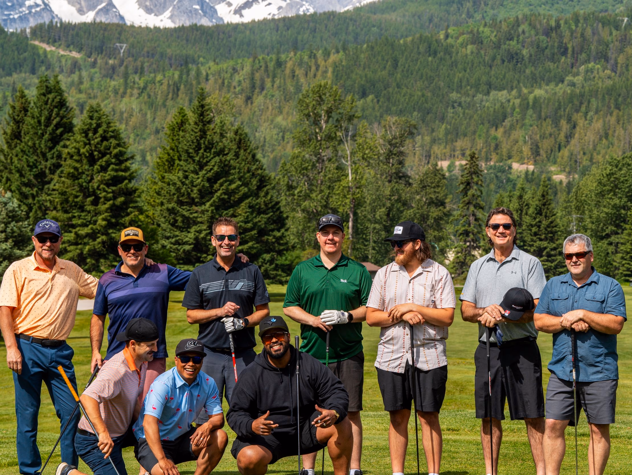 A group of golfers posing on the fairway with forested mountains behind