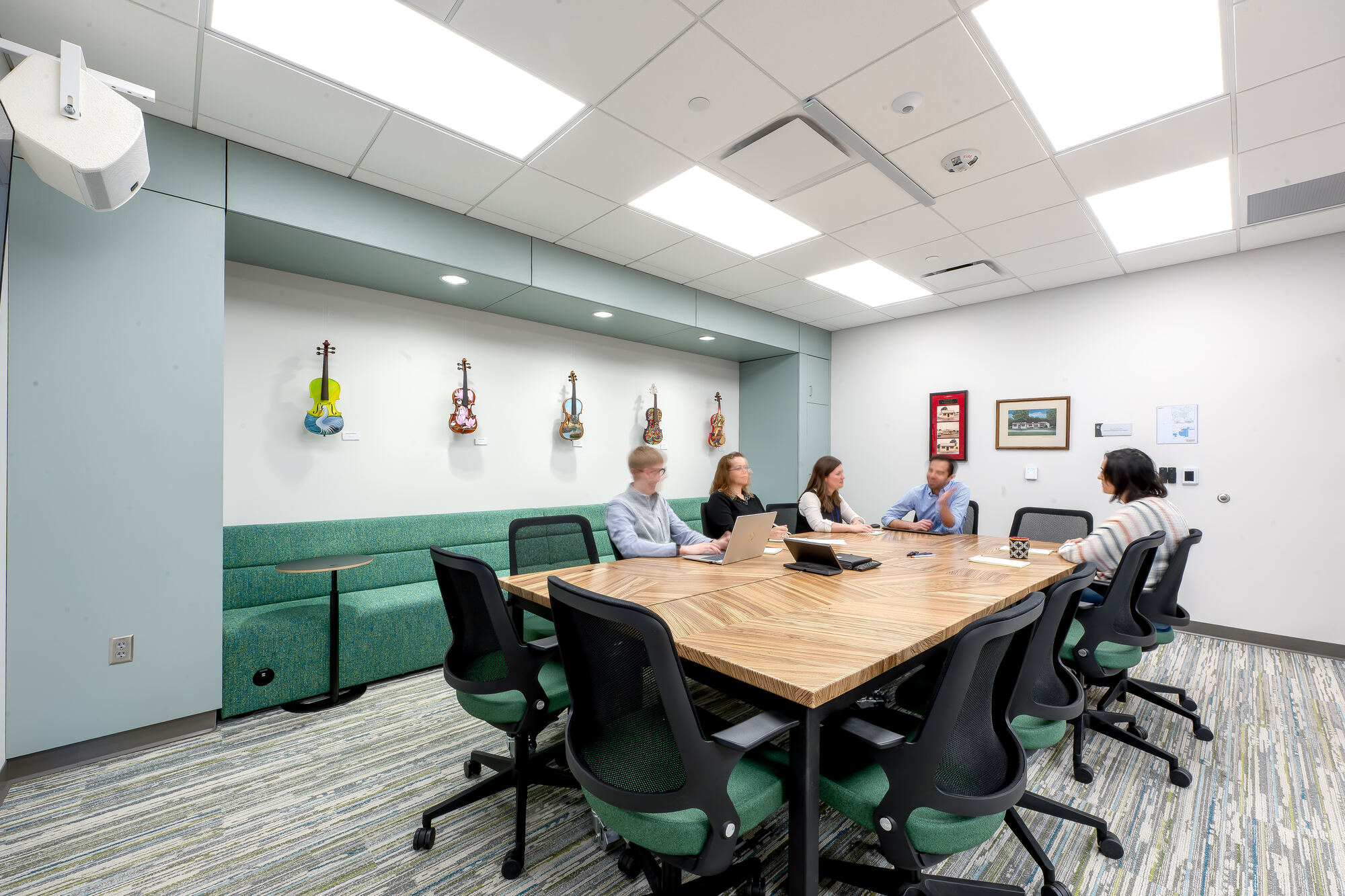 The Conference Room with a wood table, green banquette and painted violins on the wall