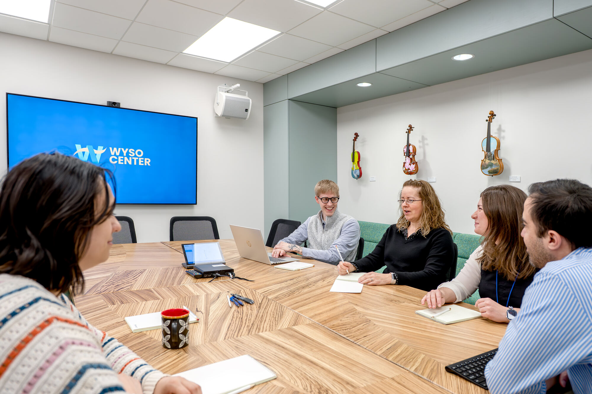 A team meeting around the Conference Room table, with a wall display