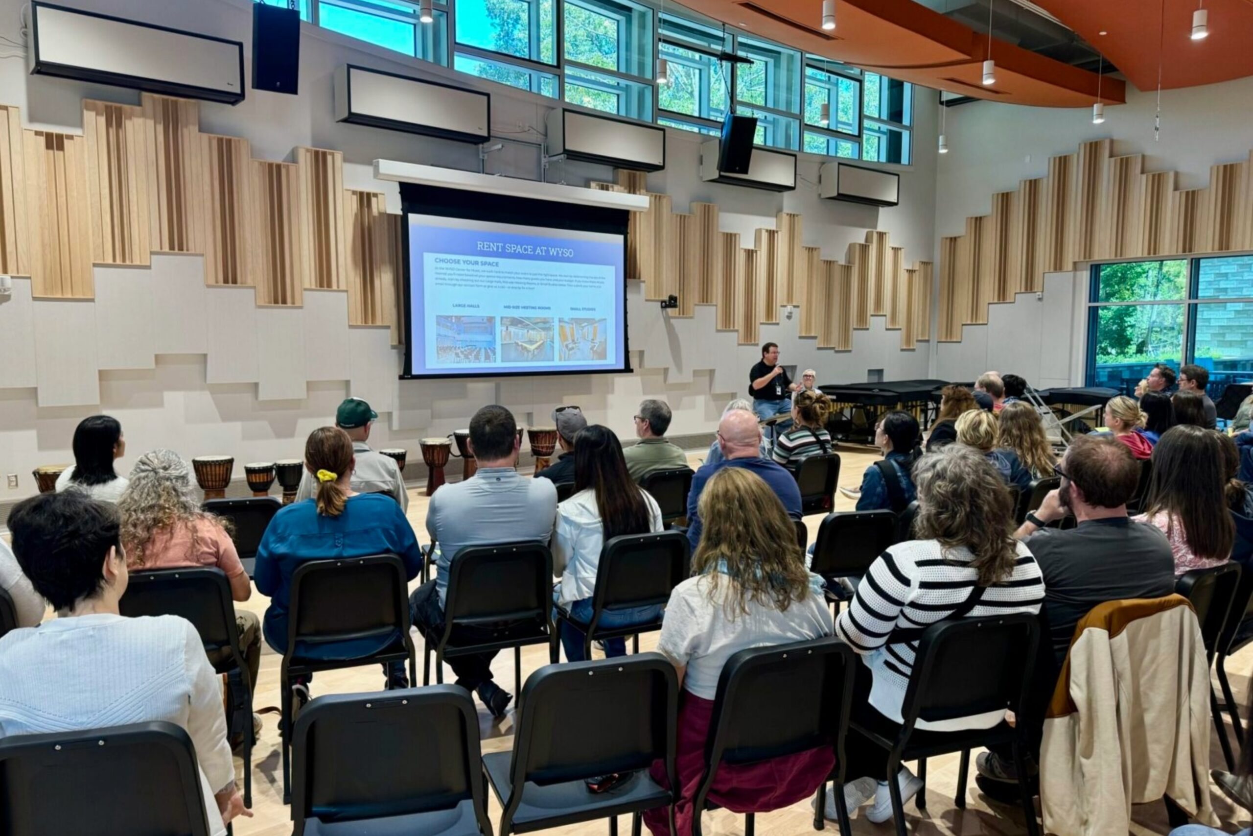 An audience in Vicki Peterson-Jenks Hall watching a presentation on the big screen