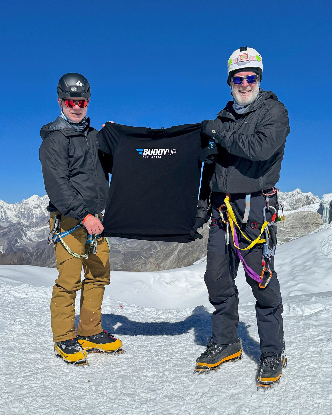 Two mountaineers displaying a Buddy Up Australia shirt on a snowy Himalayan ridge near the Khumbu Icefall.