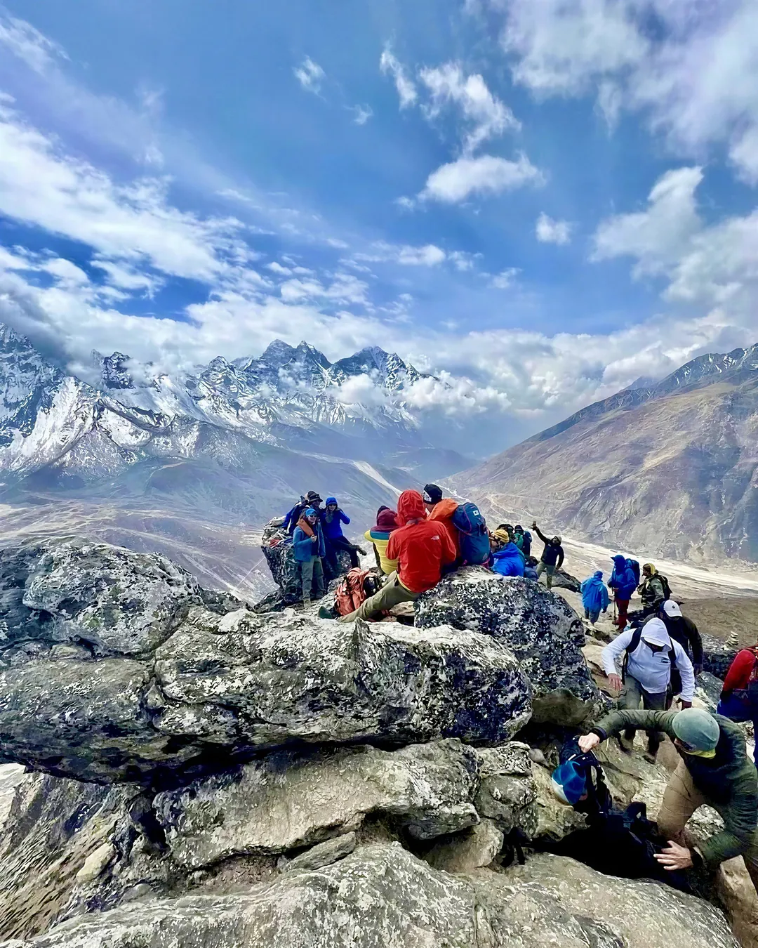 Trekkers gathered on a rocky Himalayan viewpoint overlooking snow-covered mountain peaks during an Everest Base Camp expedition.
