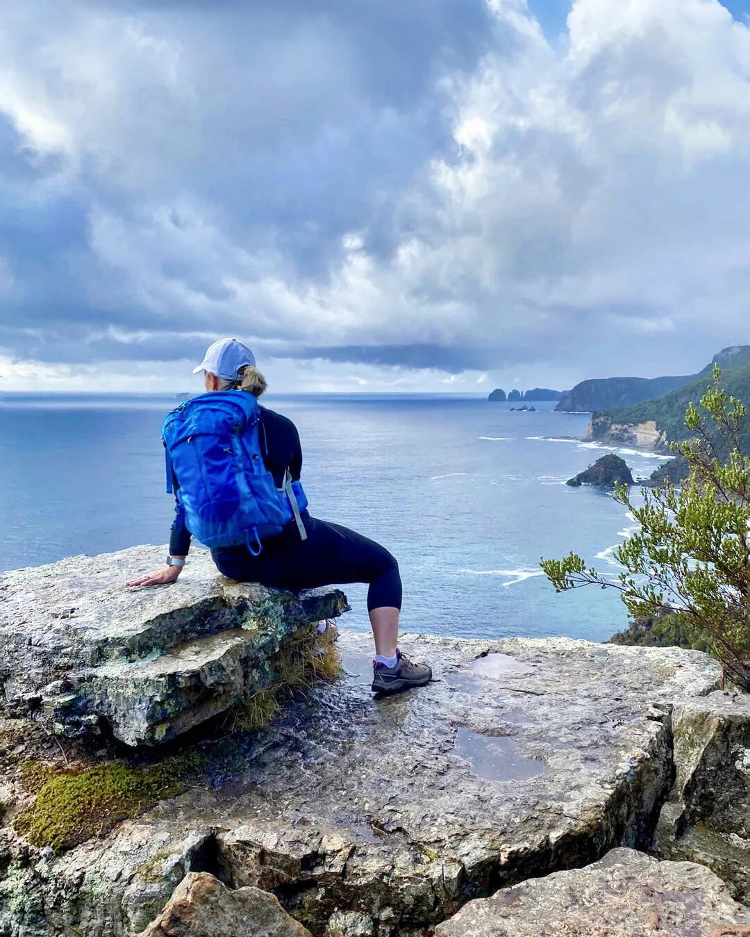Trekker seated on a rocky lookout overlooking the Tasman Peninsula coastline at Waterfall Bay, Tasmania.