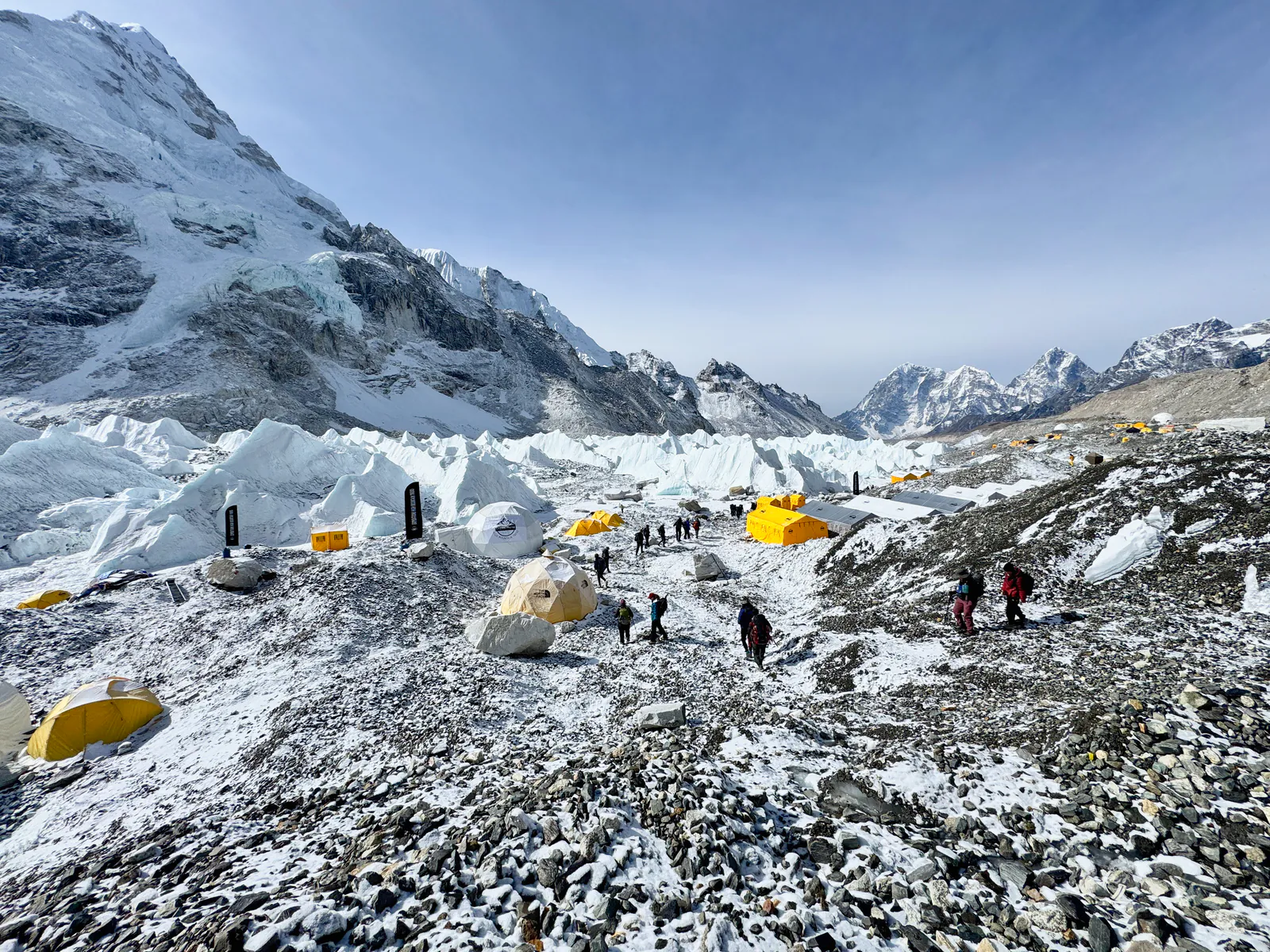 Yellow and white expedition tents beside jagged ice formations and rocky terrain at Everest Base Camp.