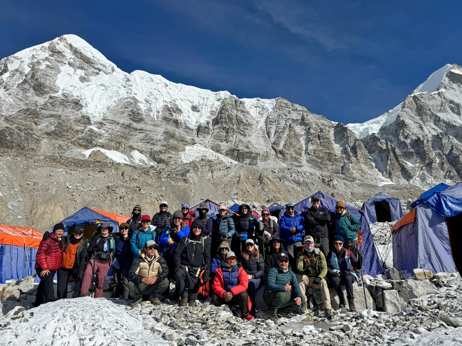 Peak Potential Adventures trekking group posing outside expedition tents at Everest Base Camp beneath snow-covered mountains.