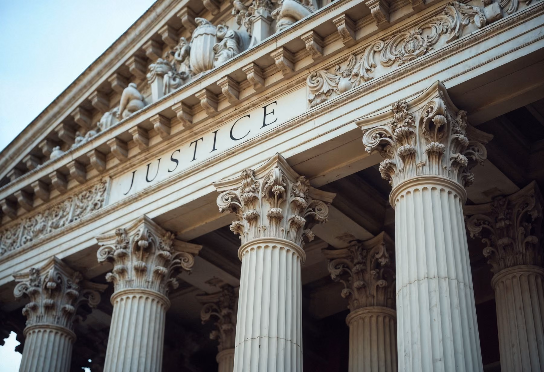 Close-up of a classical courthouse facade showing tall, ornate Corinthian columns and the word JUSTICE engraved above them.
