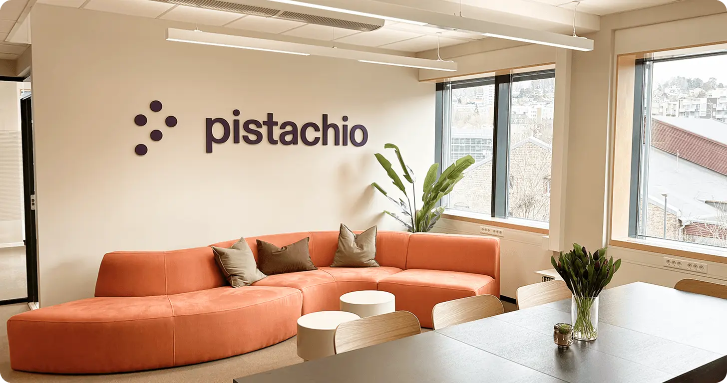 Pistachio office interior with an orange sofa, wooden tables, plants and large windows.