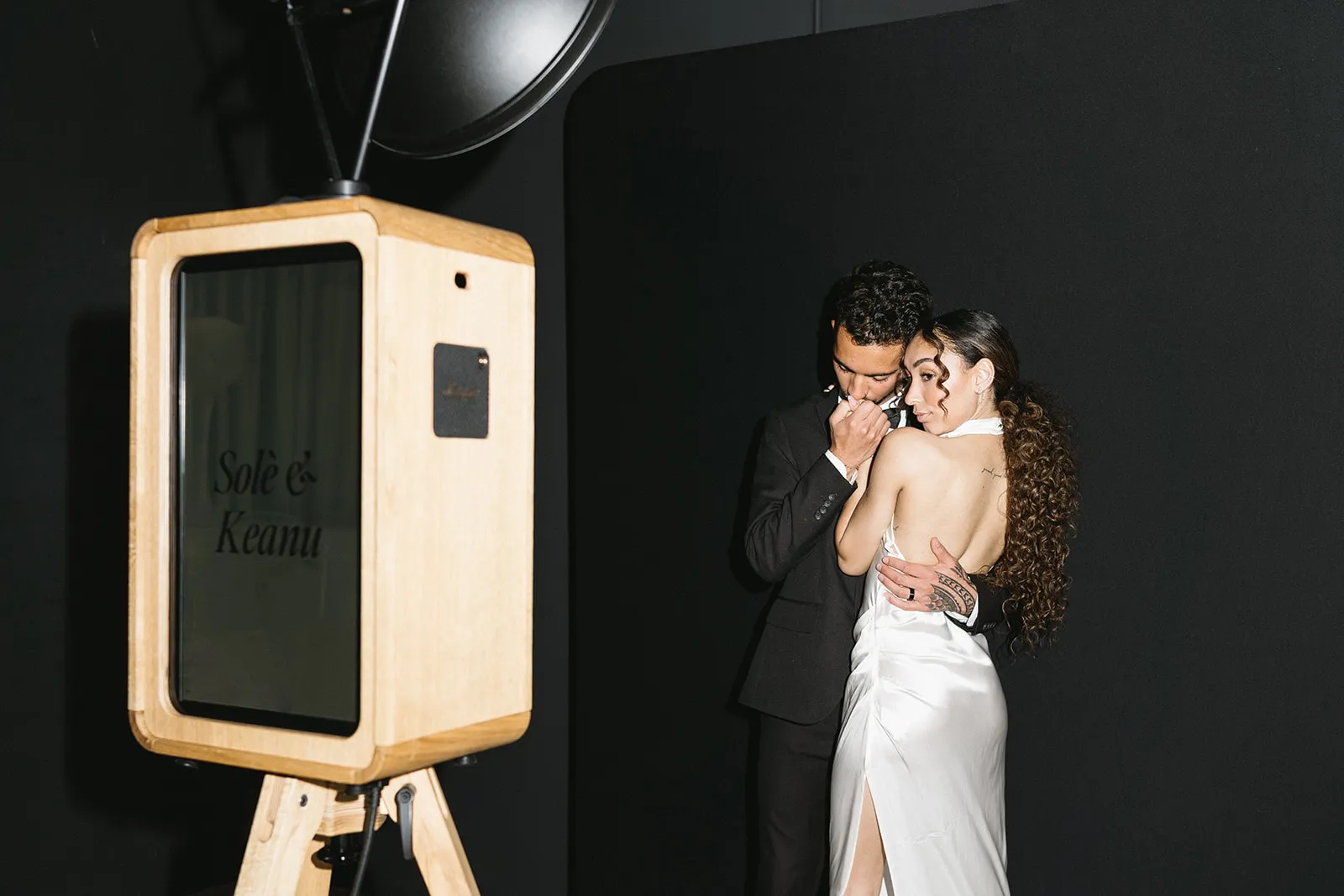 Couple embracing beside a personalised ICON photo booth screen at their wedding
