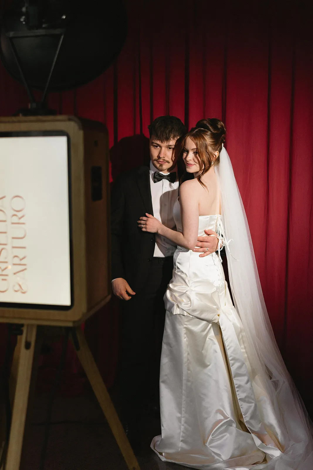 Bride and groom posing at the ICON photo booth in front of red velvet curtains