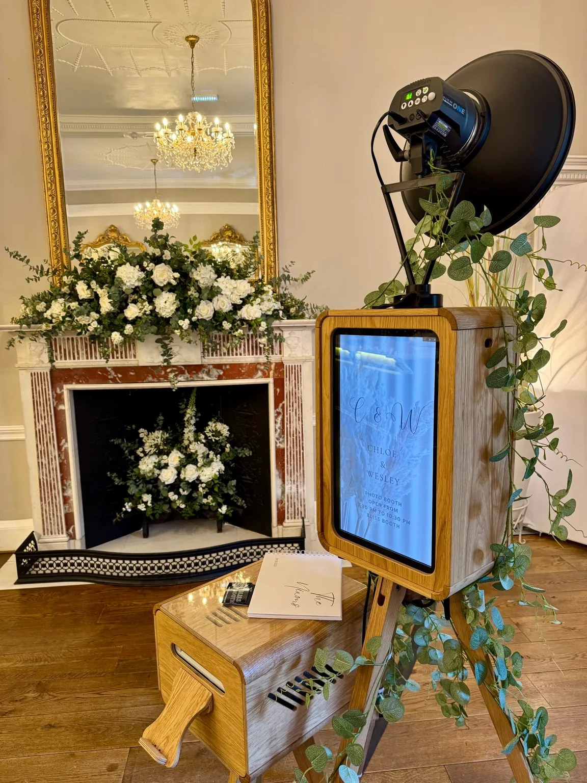 ICON photo booth dressed with eucalyptus beside a marble fireplace at a wedding venue