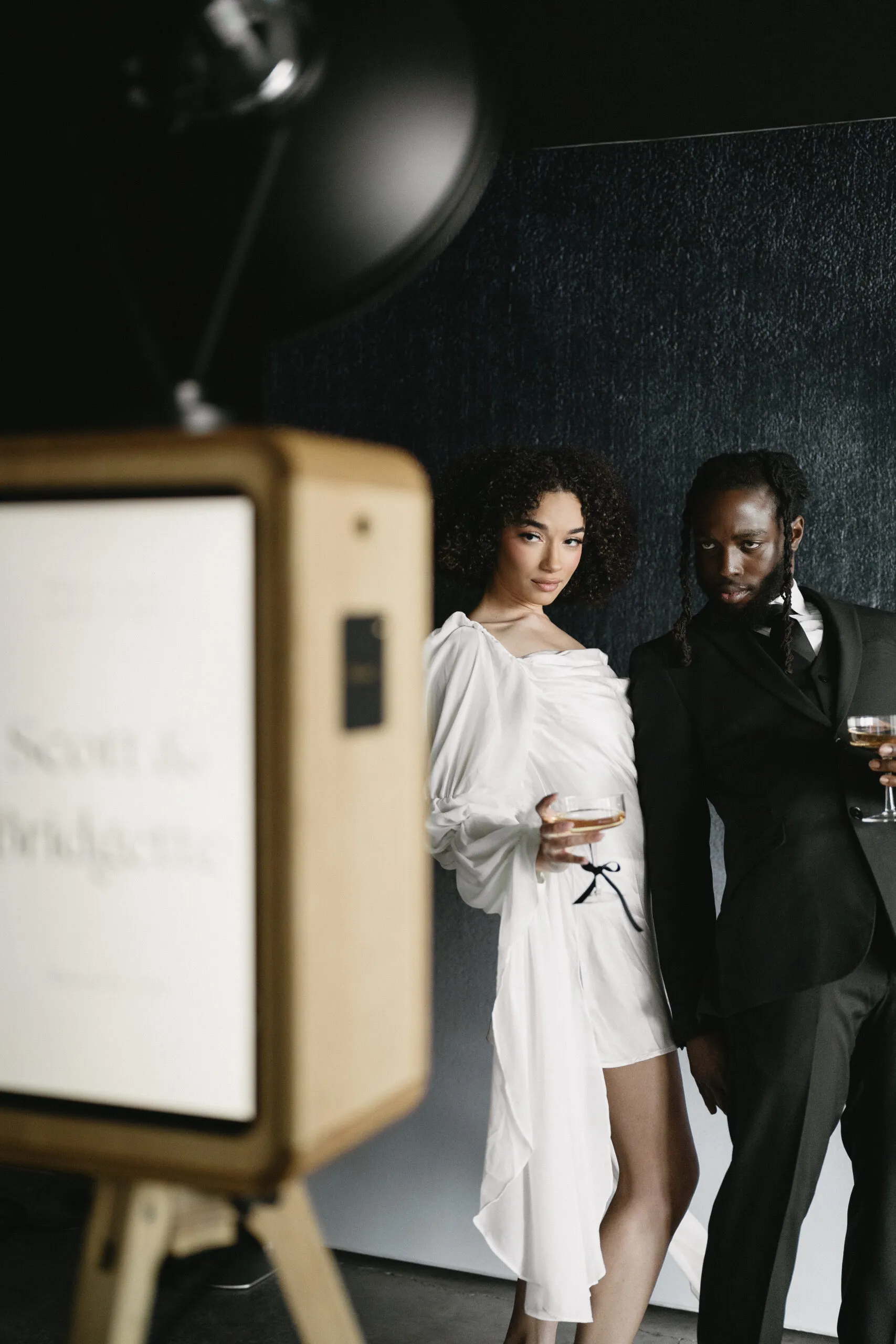 Stylish couple with champagne glasses beside a personalised ICON photo booth
