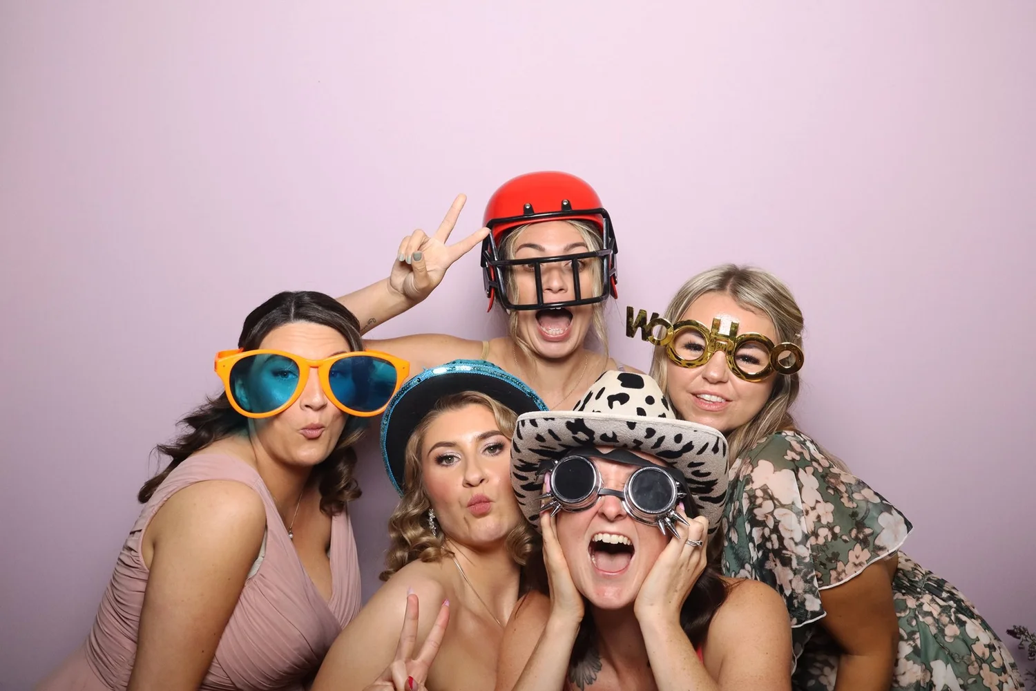 Group of friends in giant sunglasses and novelty hats having fun in the Retro photo booth