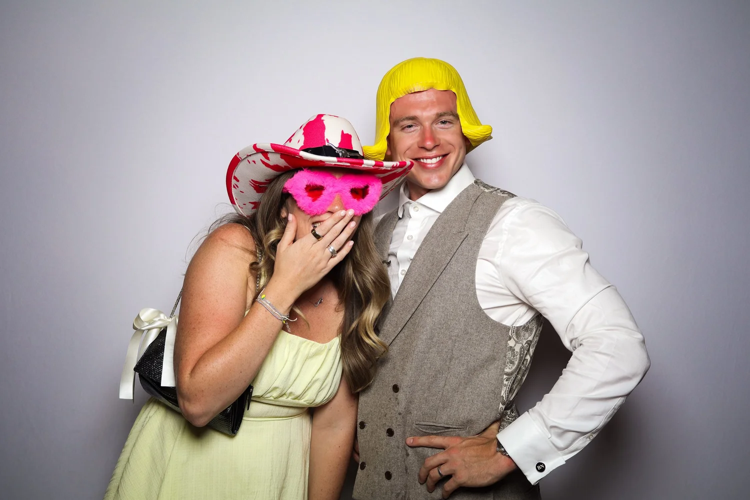 Couple wearing fun props and taking a selfie in a wedding photo booth.