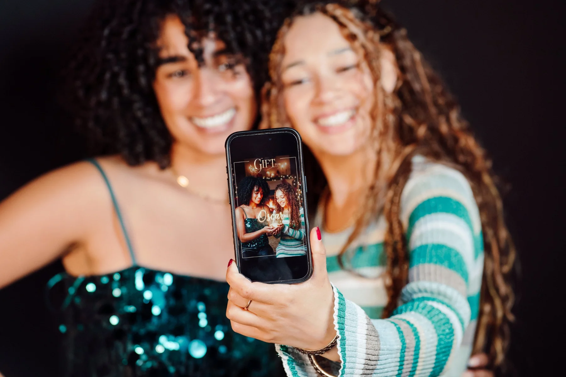 Two friends taking a selfie with their personalised festive portrait on a phone