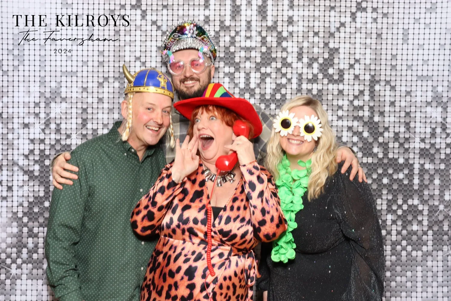 Party guests in fun hats posing against a silver sequin backdrop at the Retro photo booth