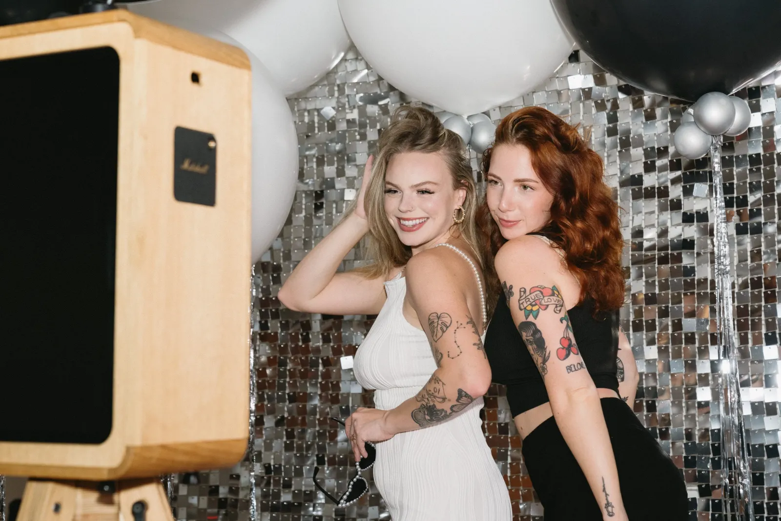 Wedding guests posing beside a wooden photo booth in front of a sequin wall