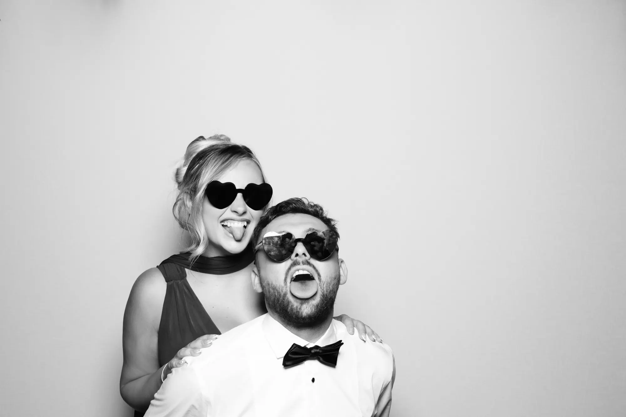 Couple pulling funny faces in heart glasses in a black and white wedding photo booth picture