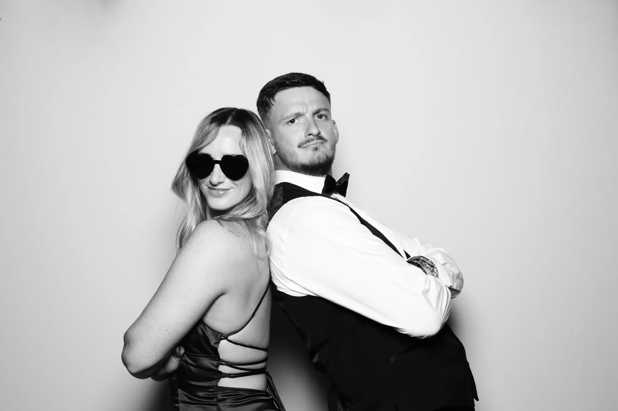 Black and white Retro photo booth photo of a couple posing back to back in heart sunglasses