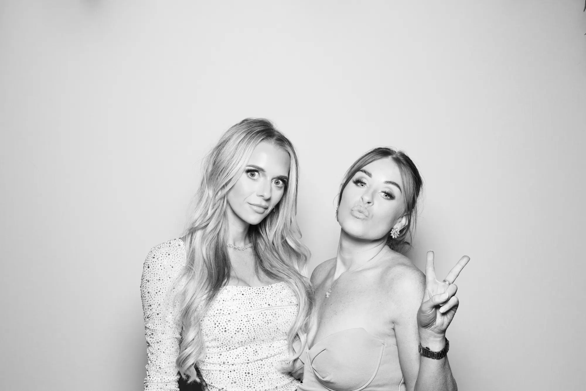 Two friends making peace signs in a black and white wedding photo booth picture
