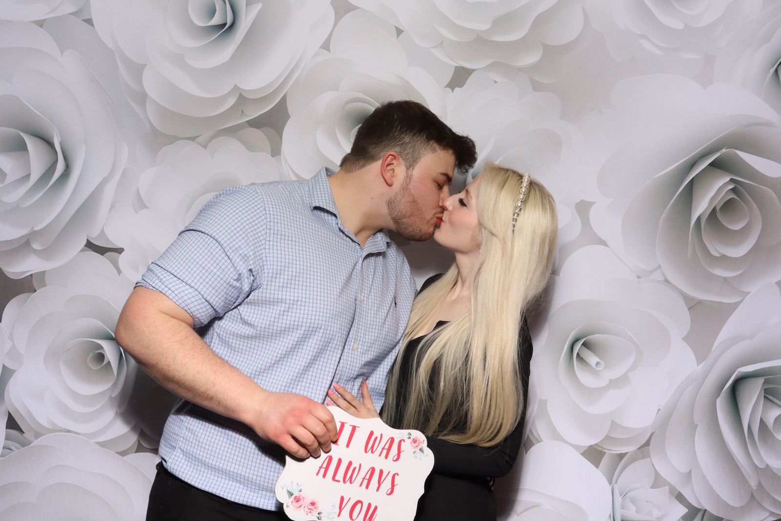 Couple kissing in front of a white rose backdrop in the Retro photo booth