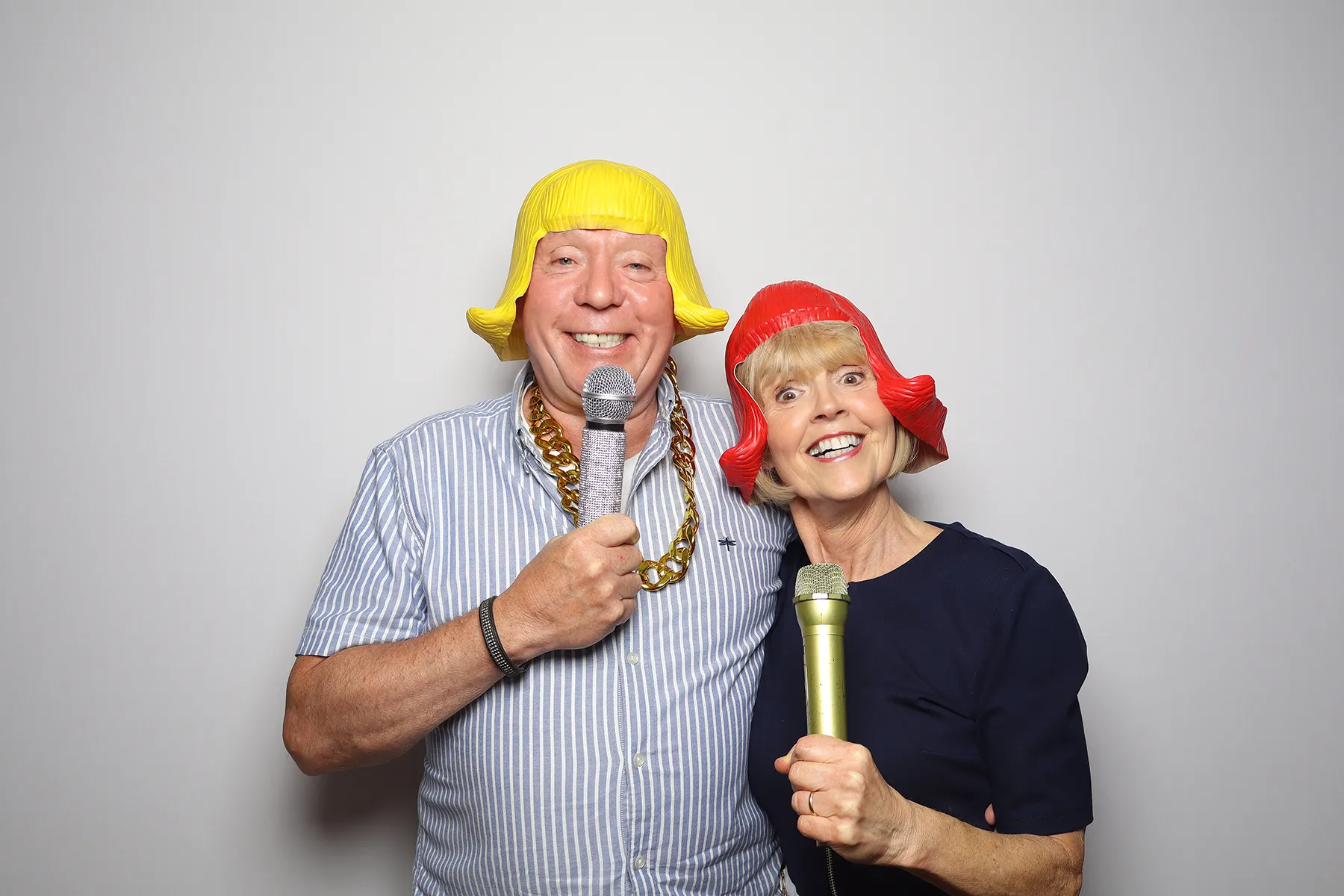 Couple in yellow and red wigs singing into microphones at the Retro photo booth