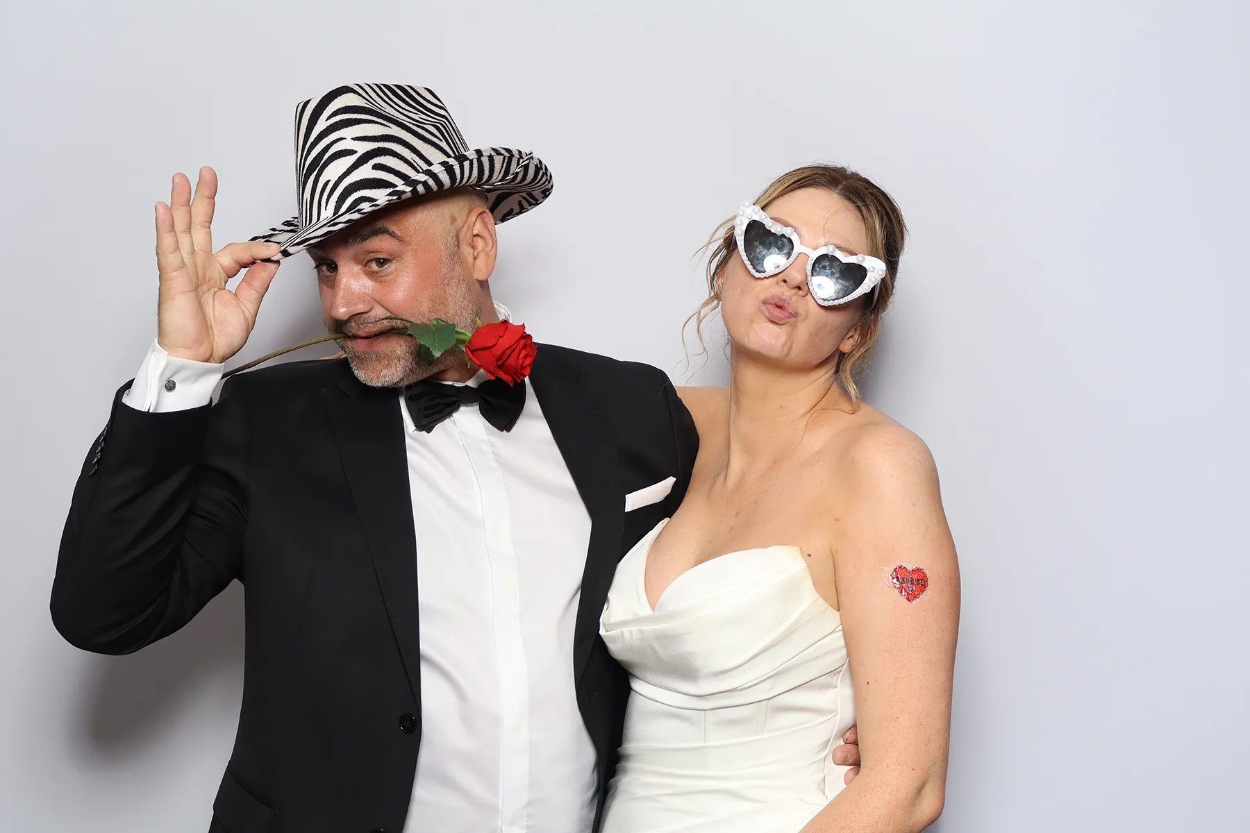Bride and groom clowning around with a rose and heart sunglasses in the Retro photo booth