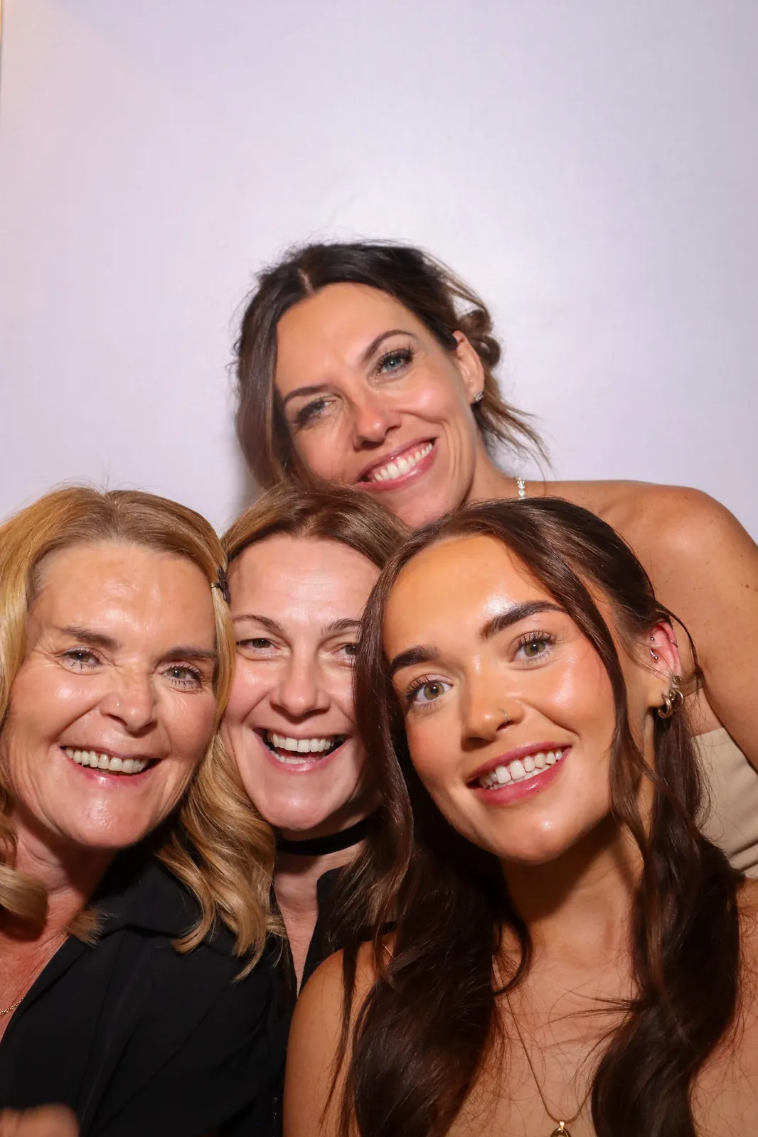 Four women smiling together in the Photomatic photo booth at a wedding