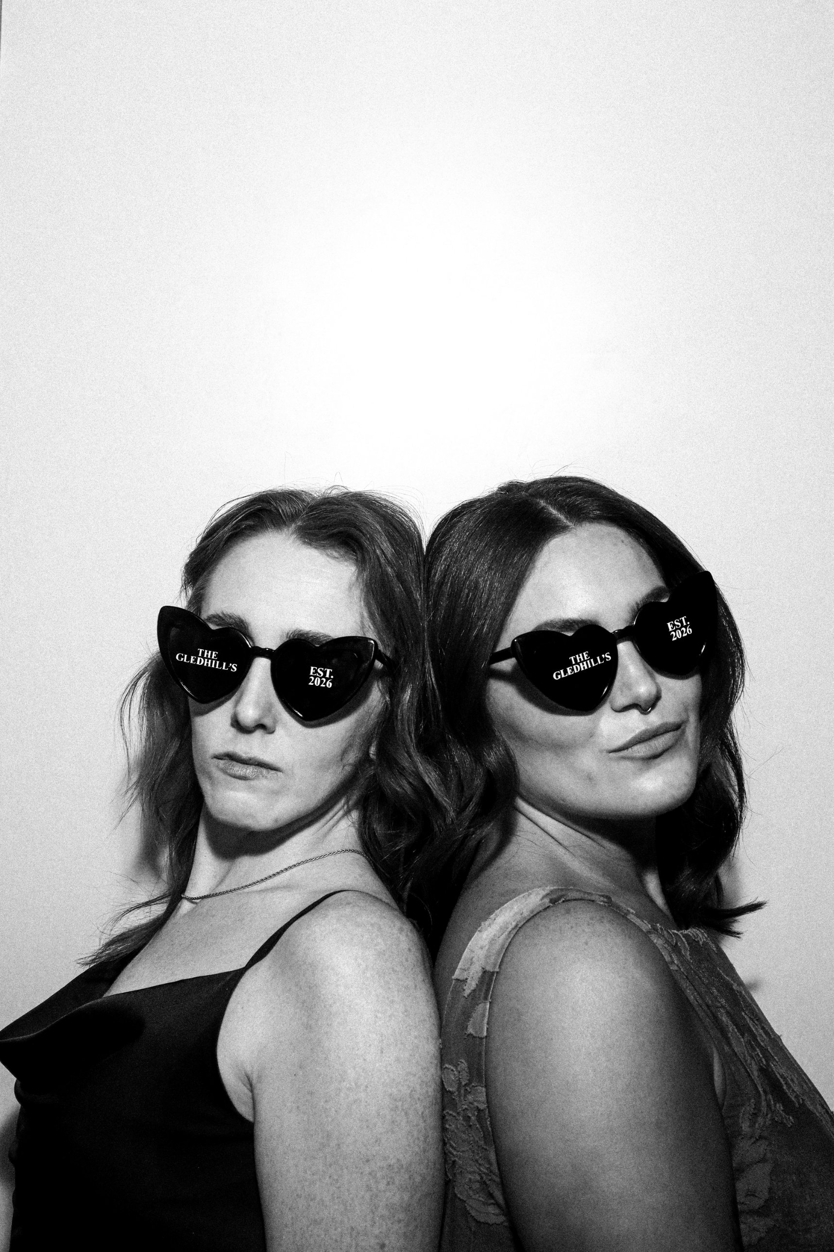 Two wedding guests back to back in personalised heart sunglasses in the Photomatic