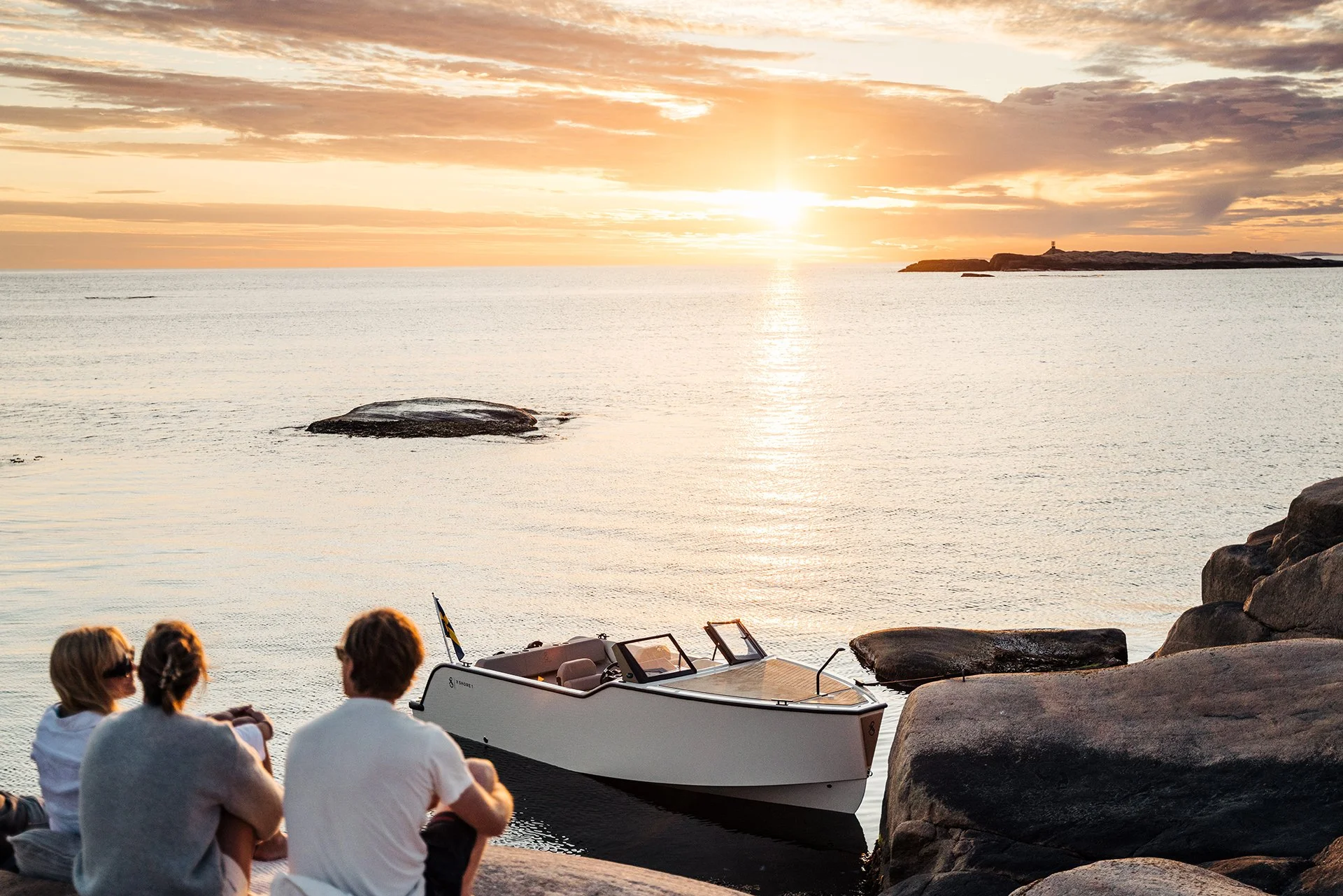 Tre personer på klippor vid en X Shore i solnedgång