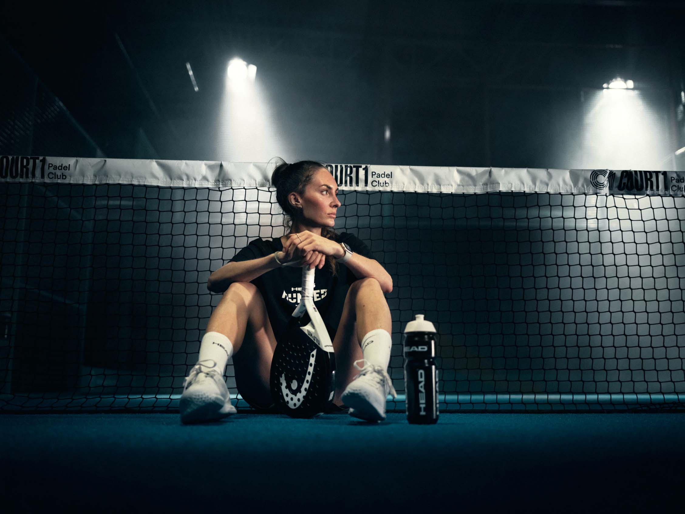 Padelspelare sitter vid nätet i strålkastarljus