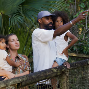 Famille de quatre personnes observant la nature avec un homme montrant quelque chose à ses enfants dans un environnement vert.