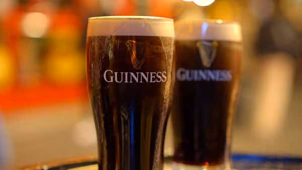 Two pints of Guinness beer with creamy heads on a reflective surface, one pint in sharp focus and the other blurred in the background.