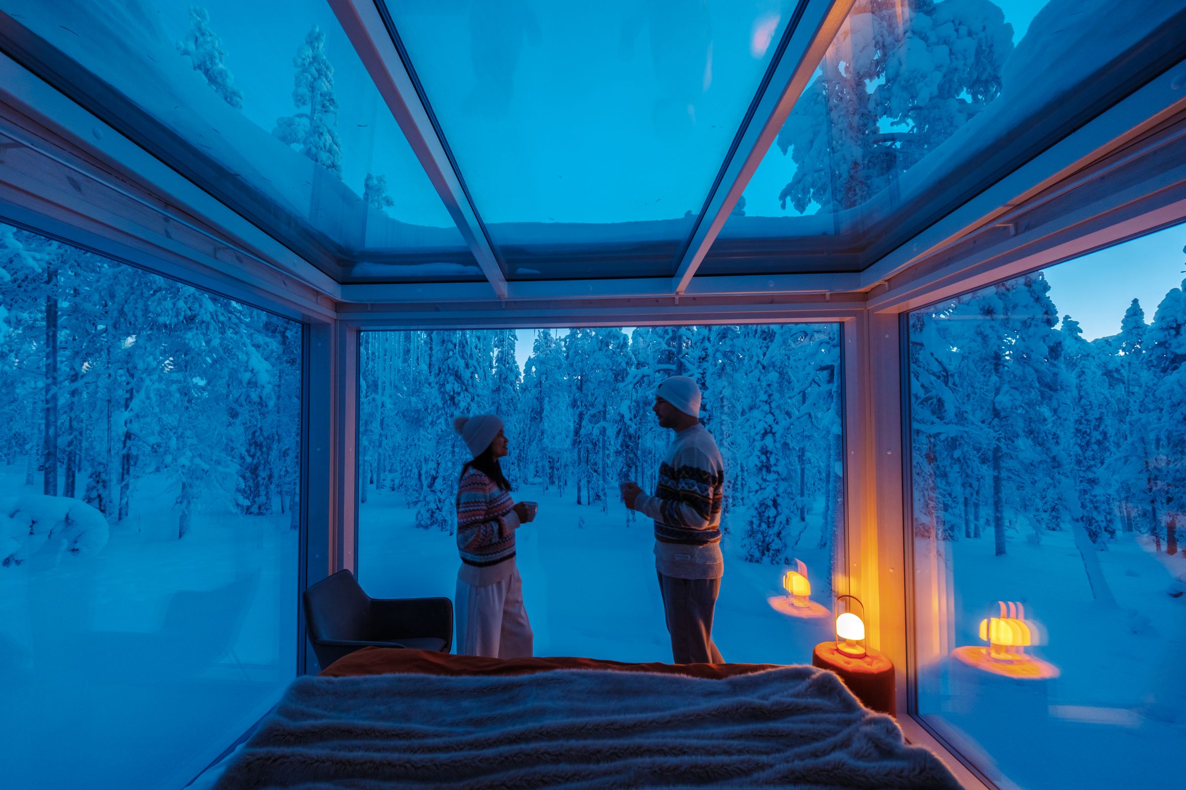 Couple in a glass cabin overlooking snowy forest in Lapland