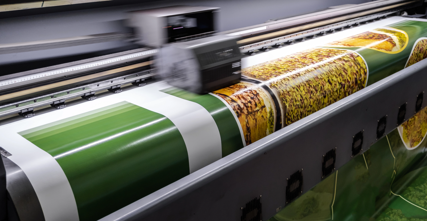 Large digital printer producing a vivid, colorful banner with green and yellow design elements.