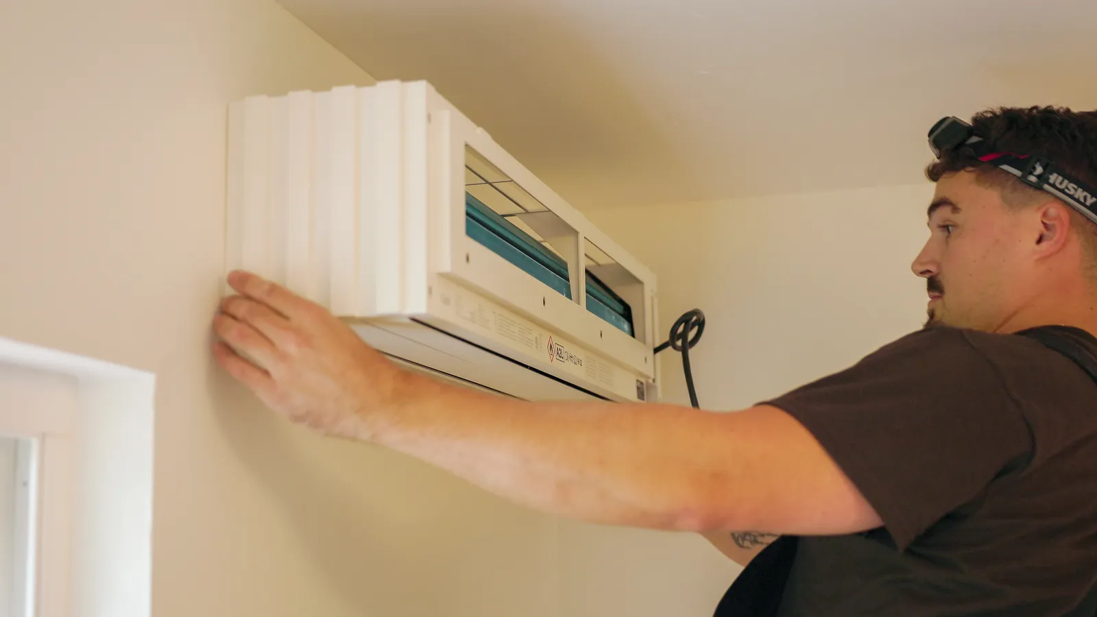 1-888-Heat-Pumps installer mounting an indoor heat pump unit on a bedroom wall