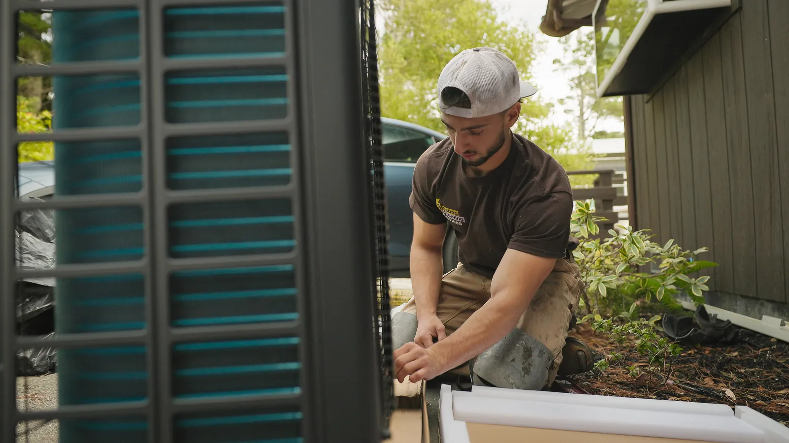 Technician installing an outdoor heat pump unit beside a house
