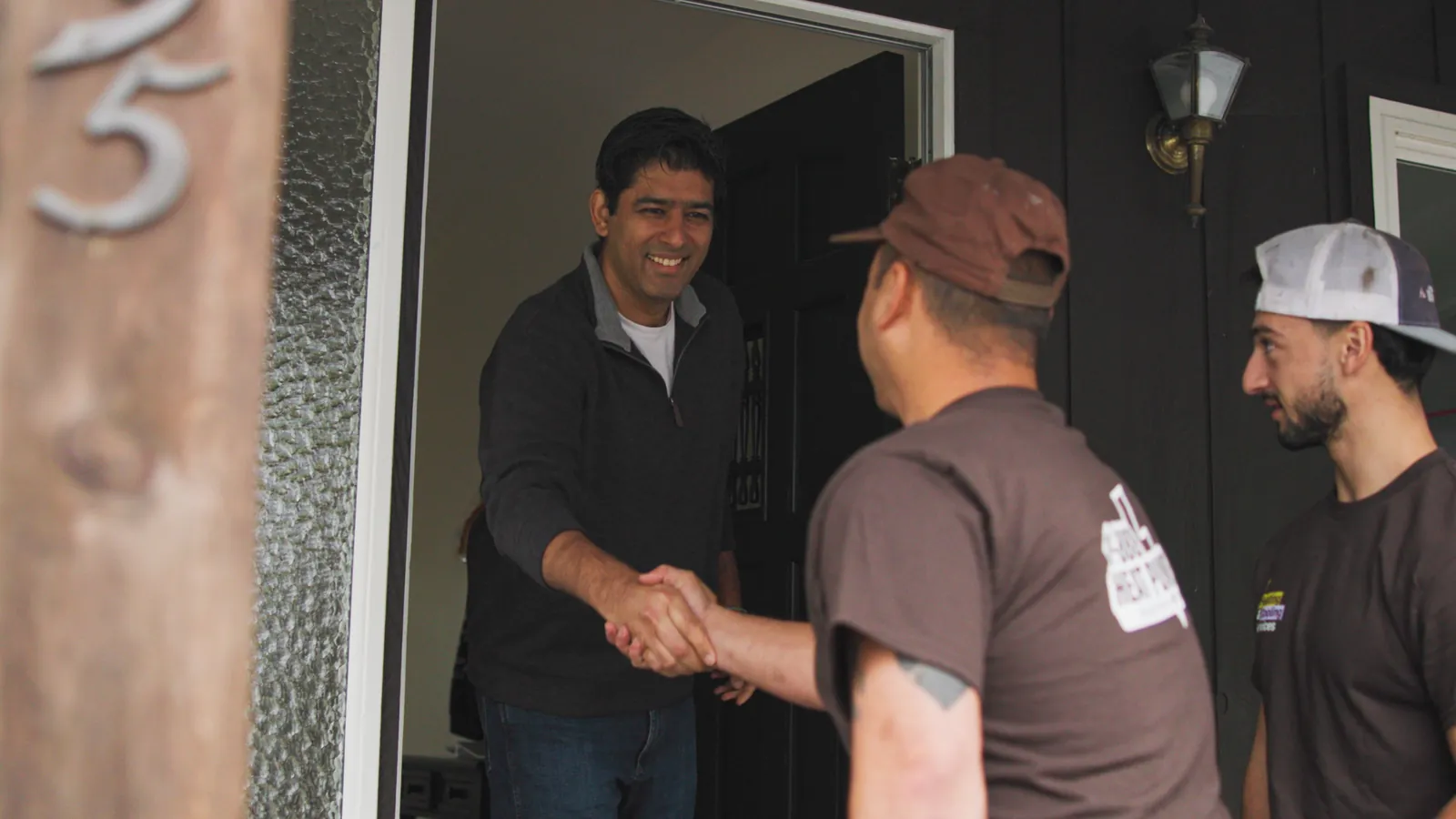 1-888-Heat-Pumps team greeting a homeowner with a handshake at the front door