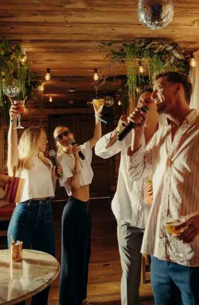 Amis chantant au karaoké à Megève, micros et cocktails à la main dans la salle boisée de Cosa Papa