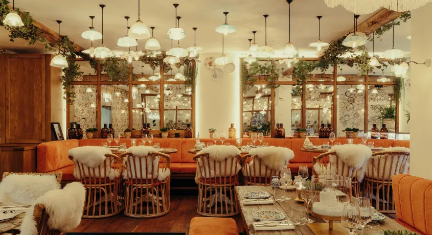 Salle du restaurant italien Cosa Papa à Megève, banquettes orange, chaises en rotin et suspensions en verre