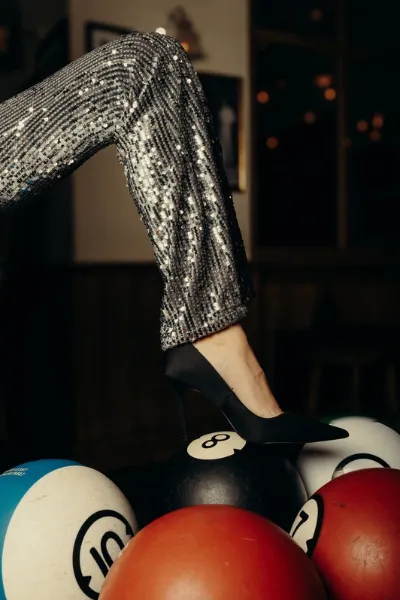 Jambe en pantalon à sequins et escarpin noir posée sur des boules colorées, ambiance festive du bowling à Megève