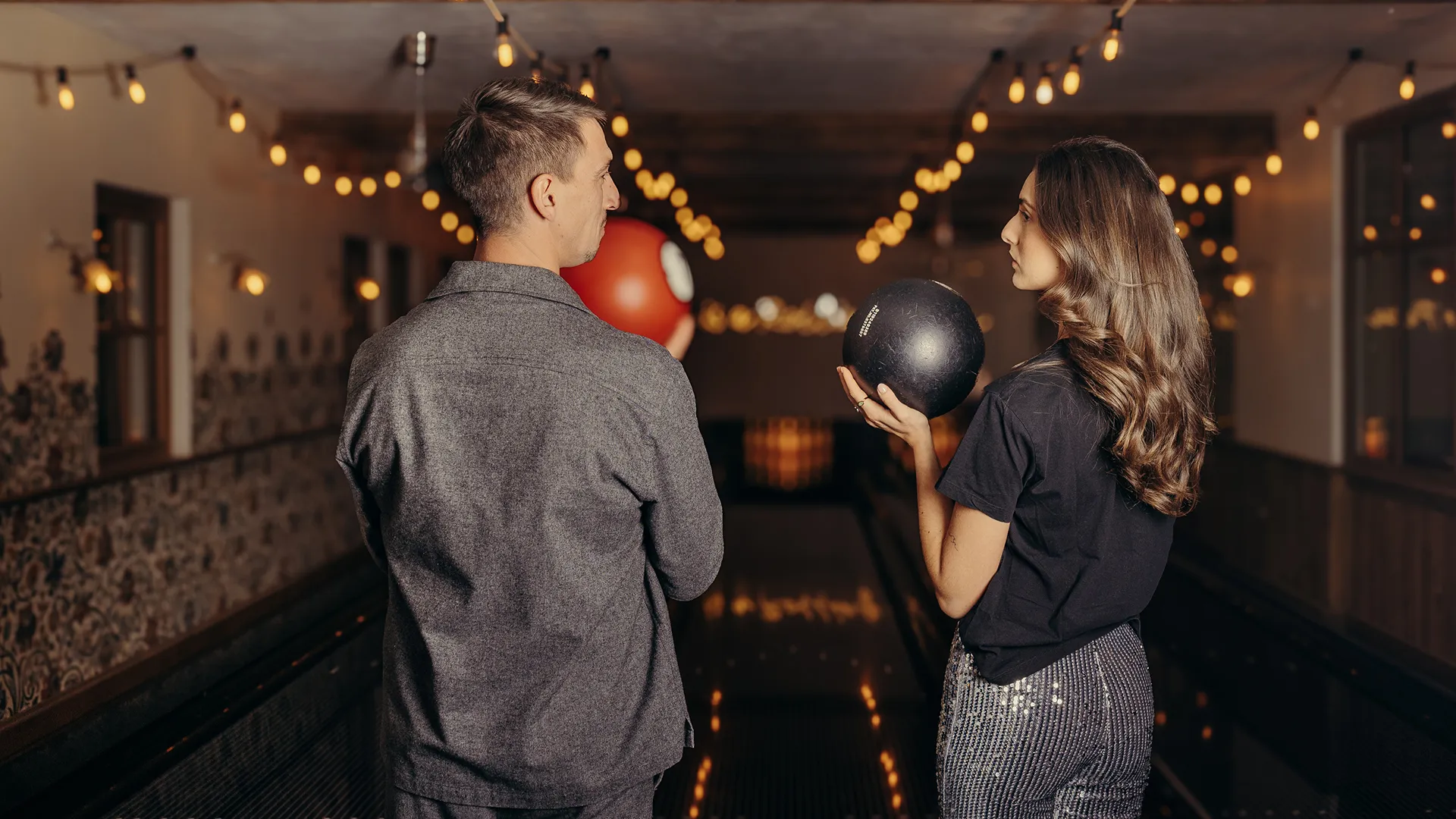 Couple tenant des boules rouge et noire sur les pistes de bowling à Megève de Cosa Papa, sous les guirlandes lumineuses