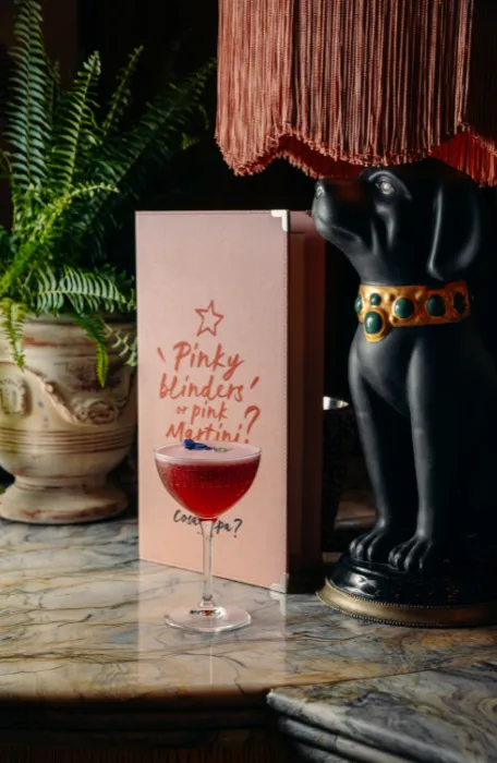 Cocktail rouge devant une carte « Pinky blinders or pink Martini? » au bar de Cosa Papa, restaurant italien à Megève