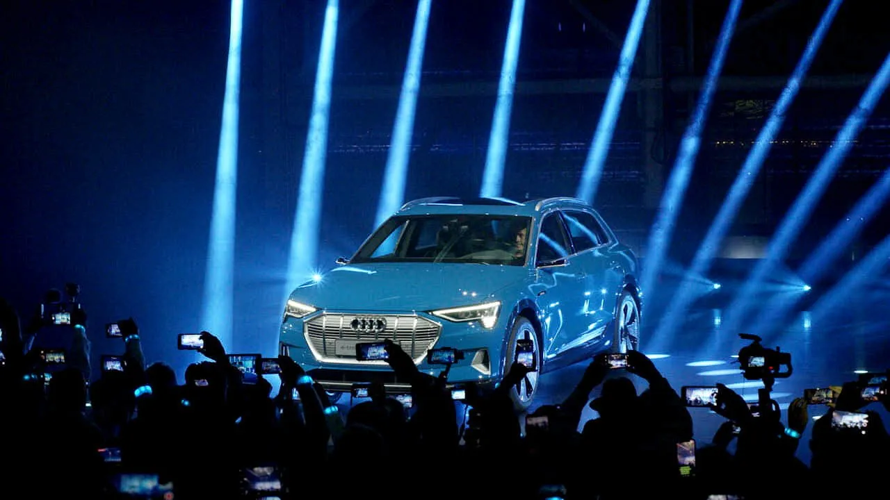 Blue Audi e-tron SUV on stage under blue spotlights as the crowd takes photos.
