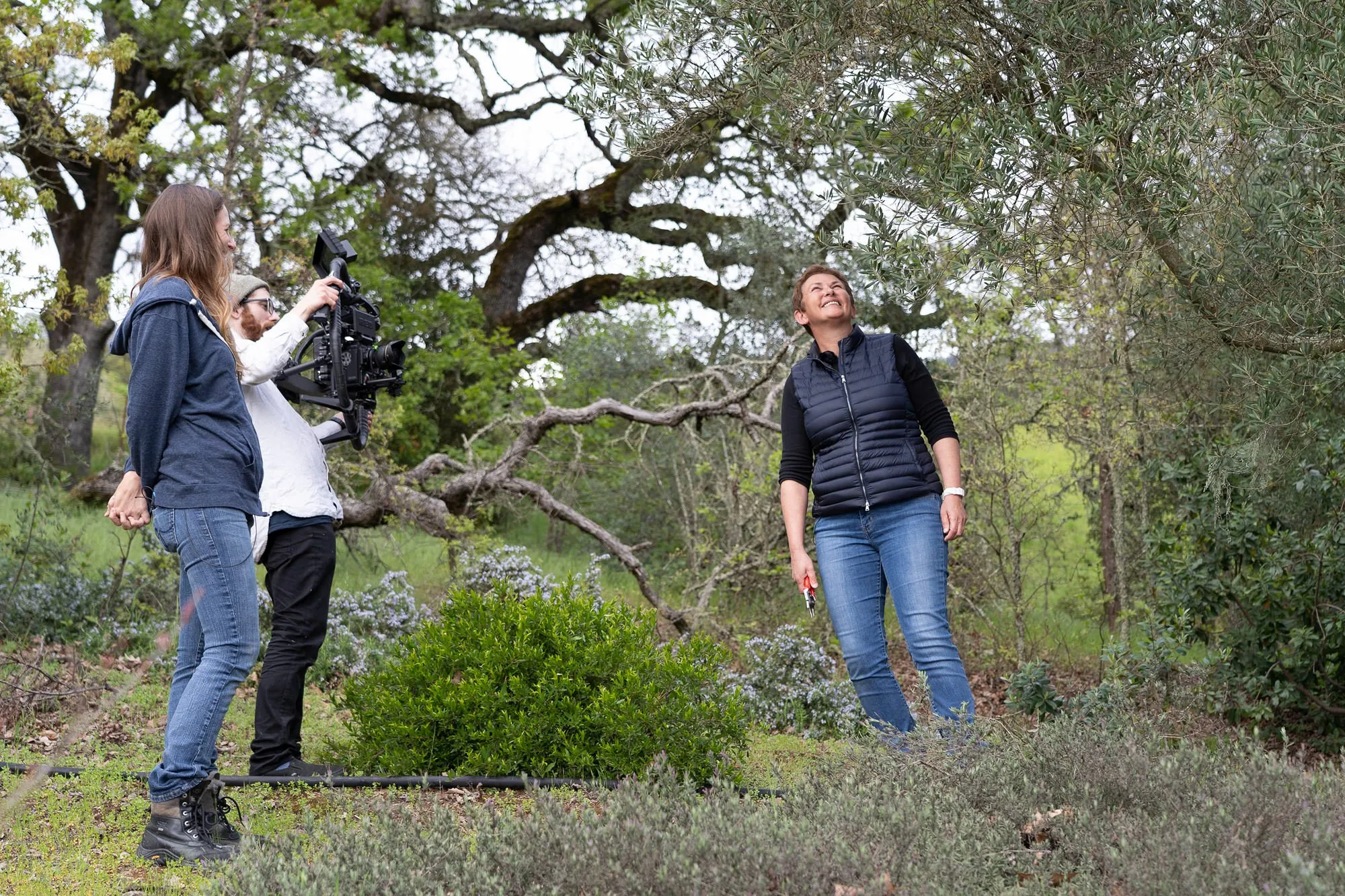 Behind-the-scenes video shoot: a crew films a woman with pruning shears in a garden.