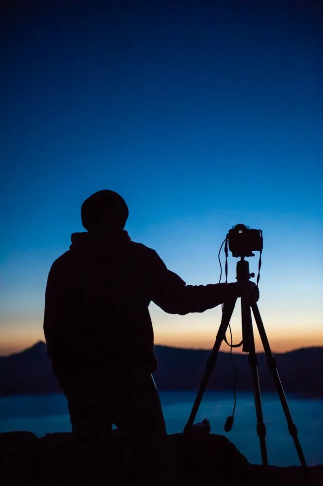 Silhouette of a person with a camera on a tripod during sunset