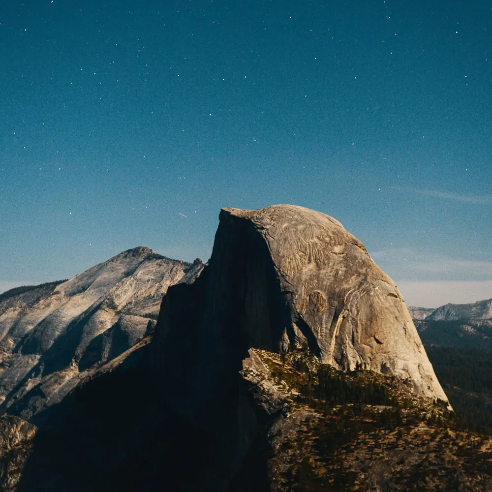 Half Dome, a prominent granite mountain peak in Yosemite National Park, illuminated under a starry night sky.
